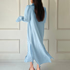 Woman wearing a light blue dress standing against a white paneled wall.