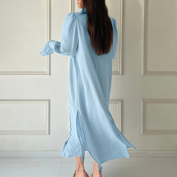 Woman wearing a light blue dress standing against a white paneled wall.