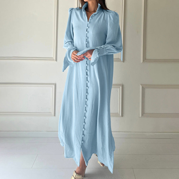 Woman wearing a light blue dress with long sleeves against a white paneled wall.