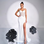 Woman in a white lace evening gown standing against a neutral background with black rocks.