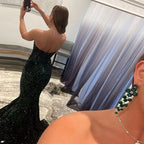 Woman in a black sequin gown taking a mirror selfie with green earrings.