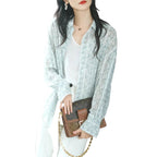 Woman holding a brown handbag with gold chain, wearing a light blue floral lace blouse.