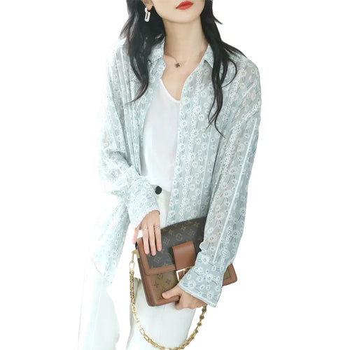 Woman holding a brown handbag with gold chain, wearing a light blue floral lace blouse.