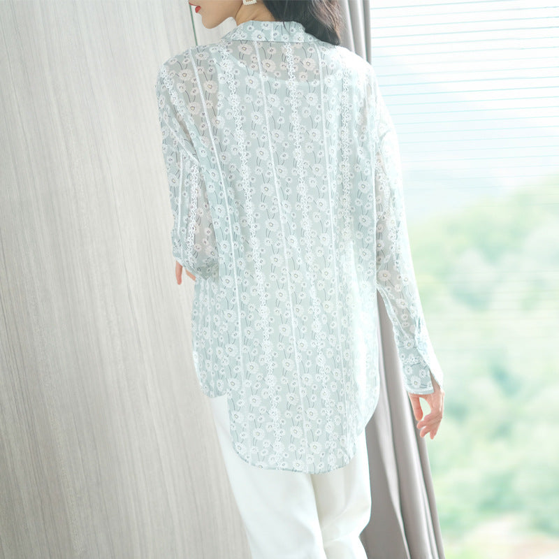 Person wearing a light blue floral lace blouse with white pants, standing in a softly blurred indoor setting.