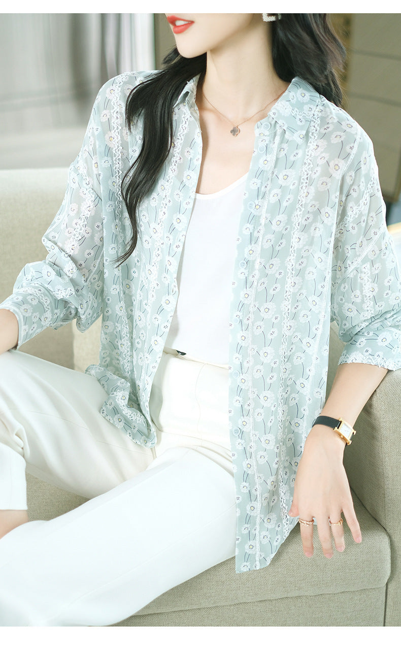 Woman wearing a light blue floral blouse over a white top and pants, sitting on a couch.