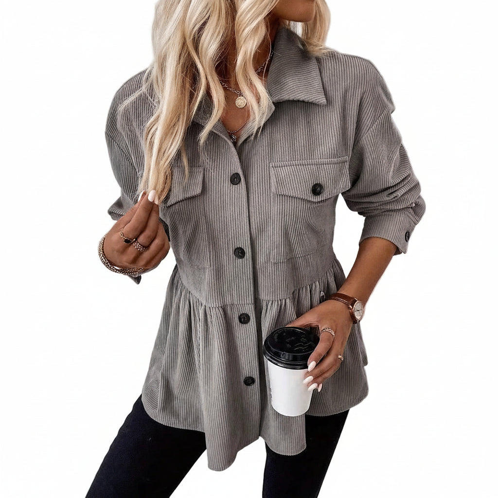 Woman wearing a gray corduroy shirt holding a coffee cup against a white wall.