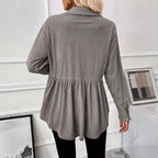 Person wearing a gray ribbed blouse in a room with white walls and framed pictures.