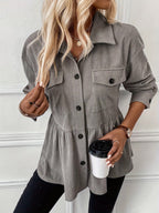 Woman wearing a gray corduroy shirt holding a coffee cup against a white wall.