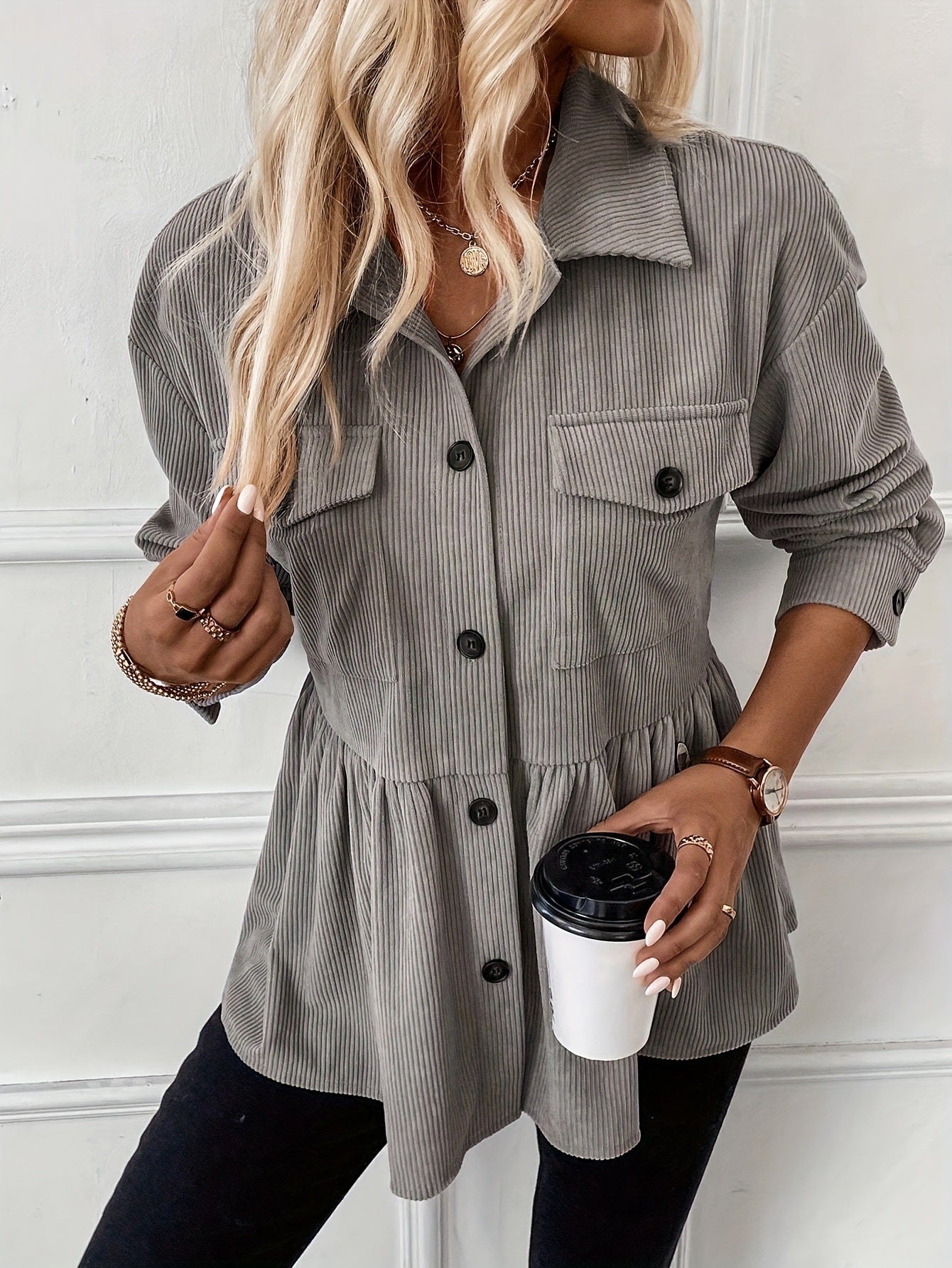 Woman wearing a gray corduroy shirt holding a coffee cup against a white wall.
