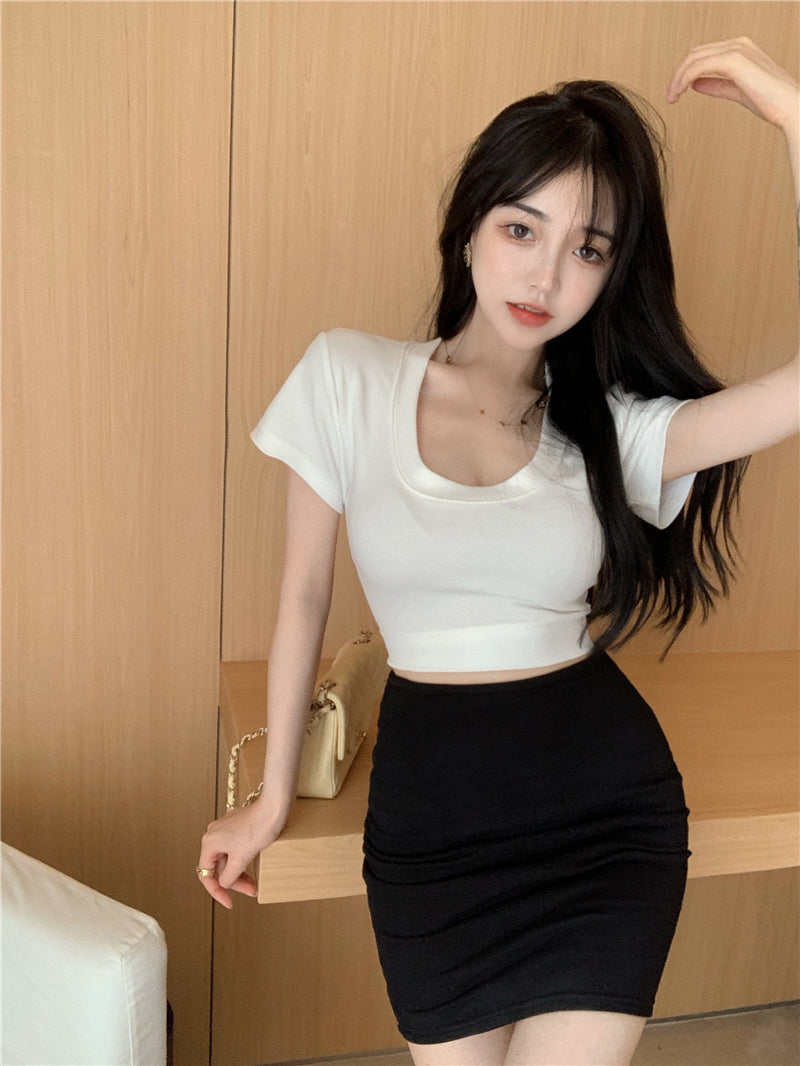Woman wearing a white crop top and black skirt against a wooden background