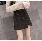Person wearing a beige sweater and plaid skirt against a gray tiled wall.