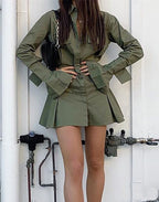 Person wearing a green outfit with a skirt and jacket against a white wall.