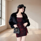 Woman in a red dress and black fur coat standing in a modern interior setting.